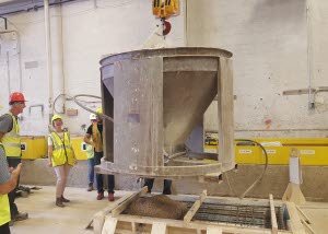 A high school teacher pours concrete into a mold with High Concrete Group co-workers.
