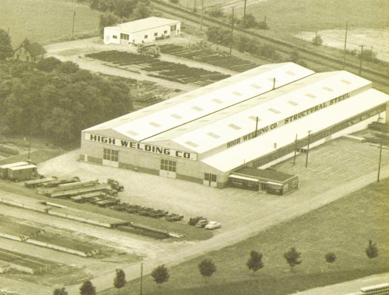 Aerial photo of High Welding Company Plant 1 in 1955 in sepia, shows the railroad behind the building and a line of newly planted trees next to the yard.